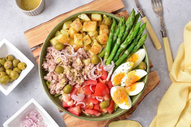 Make this salad with tomatoes, asparagus, potatoes, egg, tuna, olives, shallots, and vinaigrette