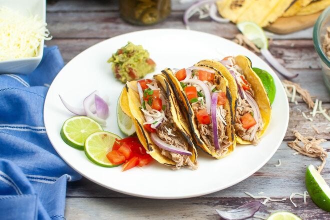 Pork carnitas in tortillas with lime, guacamole, onion, and tomato are a crowd favorite for summer dinner